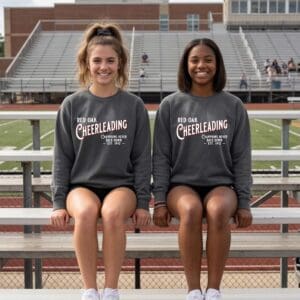 Two cheerleaders seated on bleachers smiling.